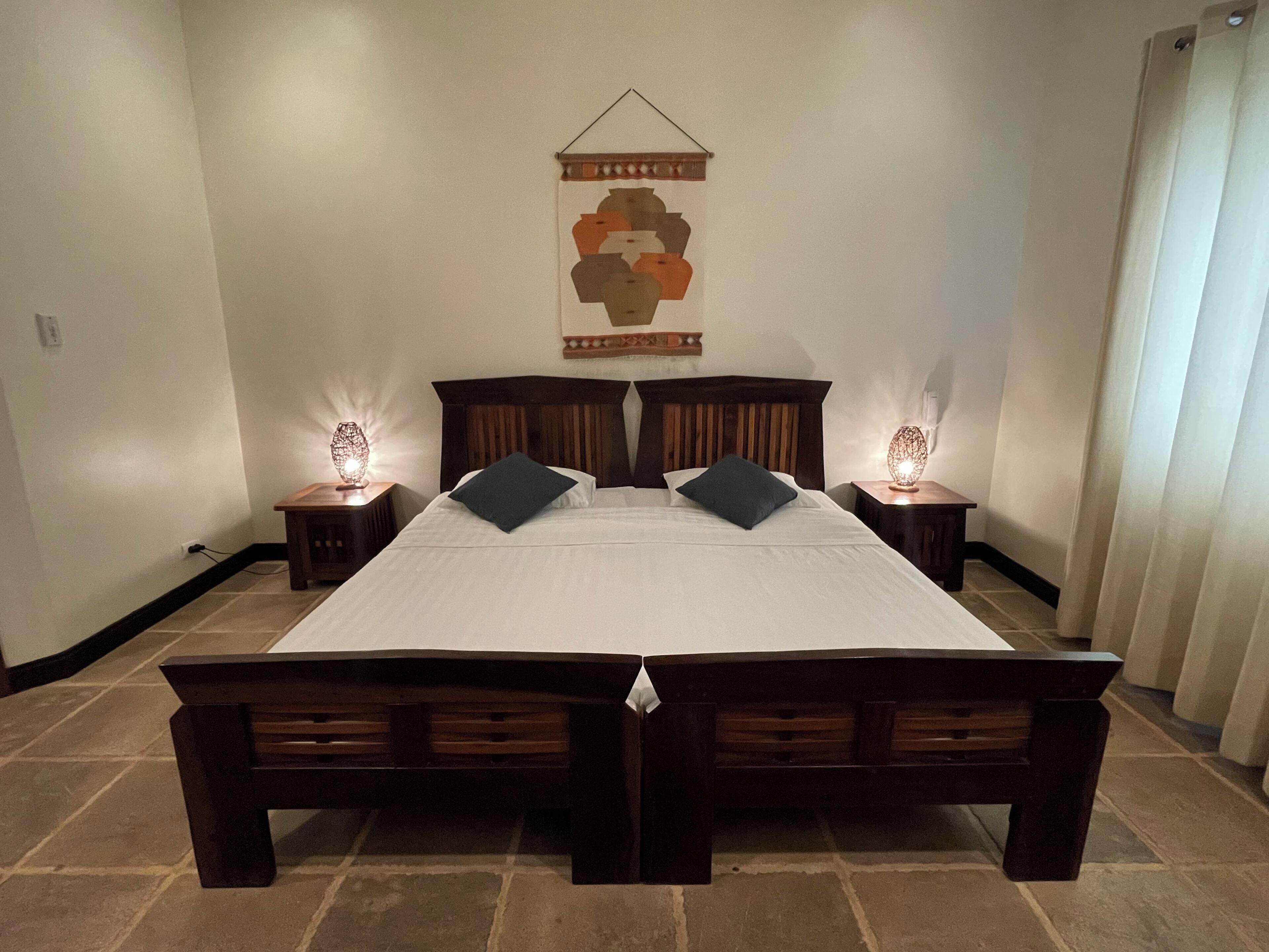 Un lit double avec une tête de lit en bois, deux tables de chevet avec des lampes et un élément décoratif mural.