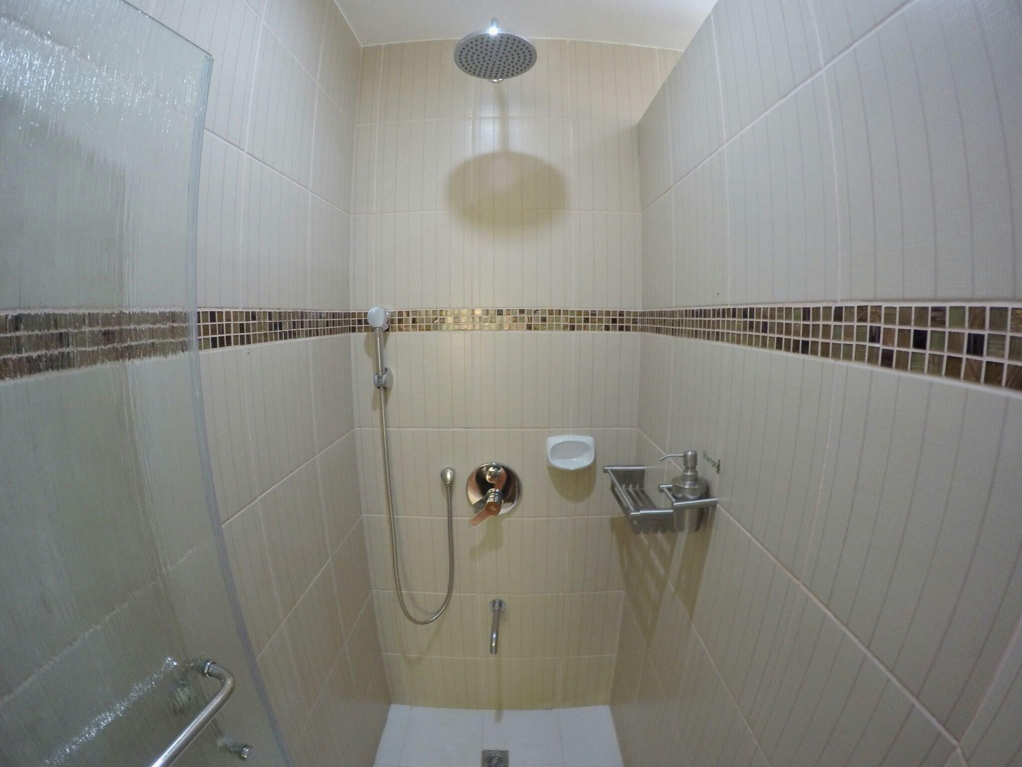 A small, tiled shower stall with a handheld showerhead, a wall-mounted toilet, and a sink.