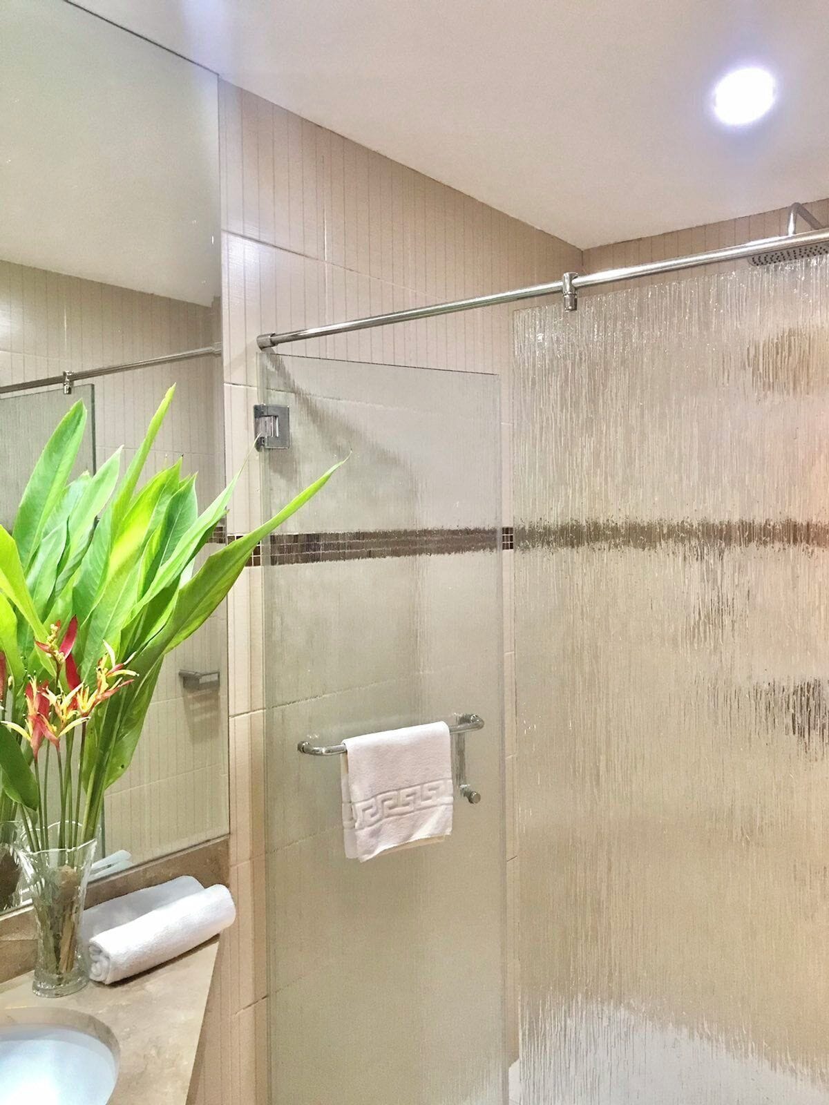 A modern bathroom with a glass shower enclosure, a towel rack, and a vase with flowers on the counter.