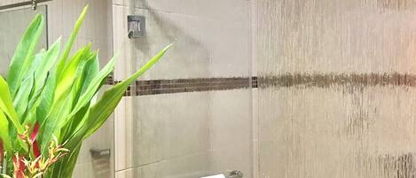 A modern bathroom with a glass shower enclosure, a towel rack, and a vase with flowers on the counter.