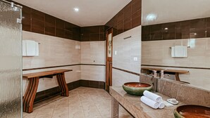 Un baño moderno con un banco, un espejo grande y dos lavamanos.