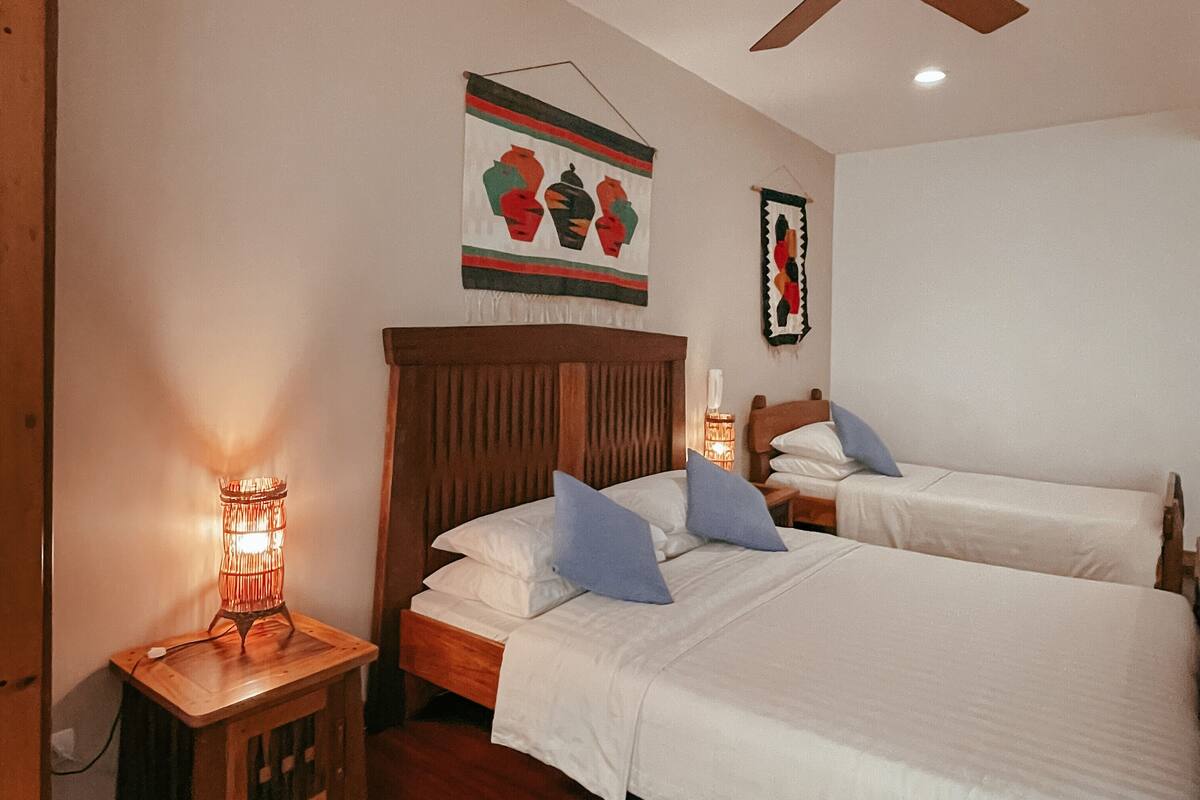 A bedroom with two beds, a ceiling fan, a nightstand with a lamp, and wall art.