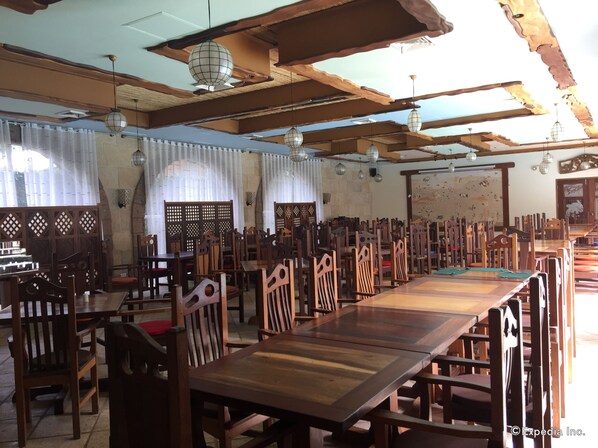 A spacious dining area with wooden tables and chairs, decorative ceiling beams, and hanging lanterns.