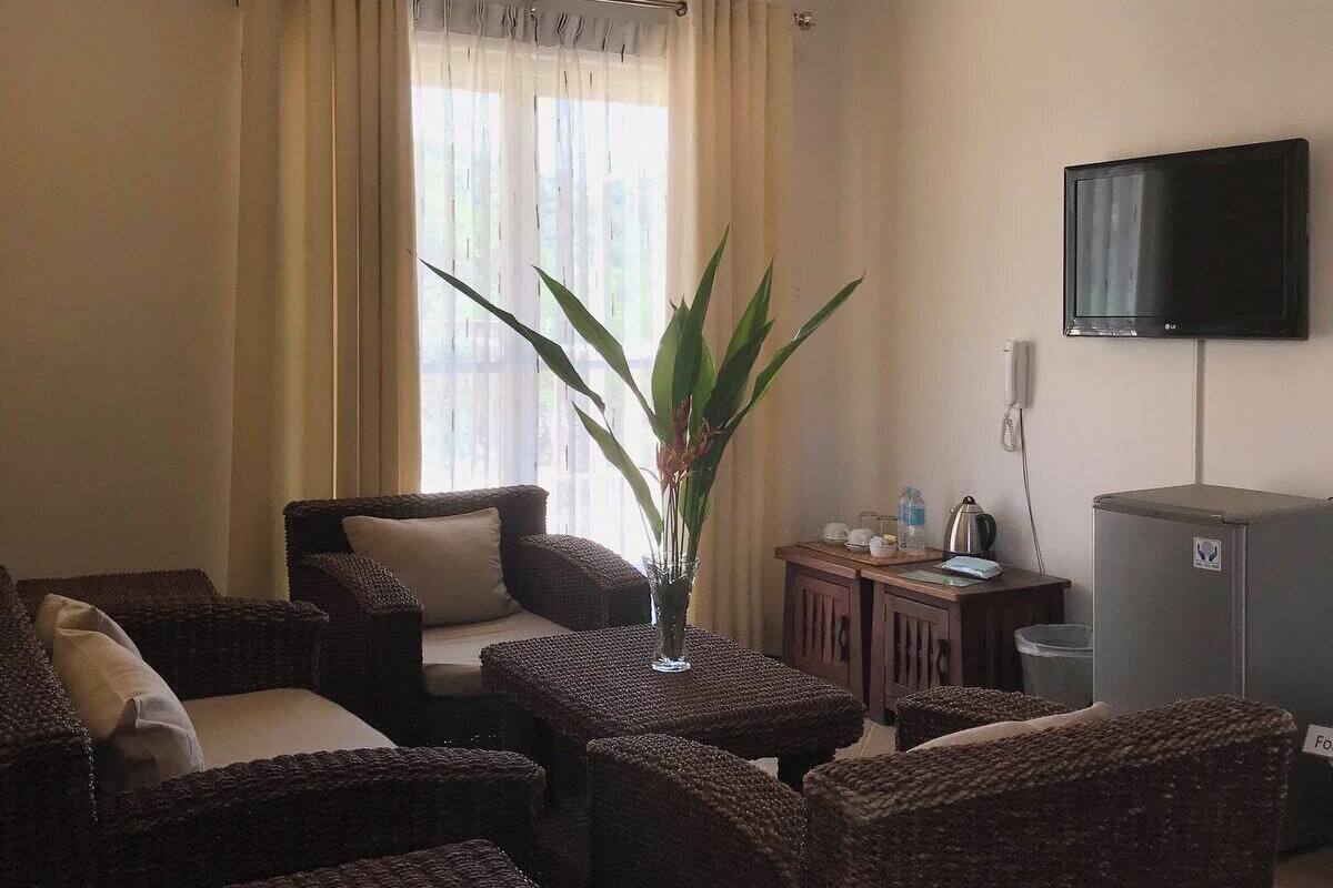 A living room with wicker furniture, a ceiling fan, a television, and a window with curtains.