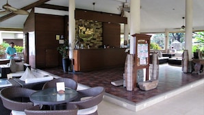 A reception area with a reception desk, a large potted plant, wicker furniture, and a stone wall with a decorative piece. - Chali Beach Resort and Conference Center (Cagayan de Oro)