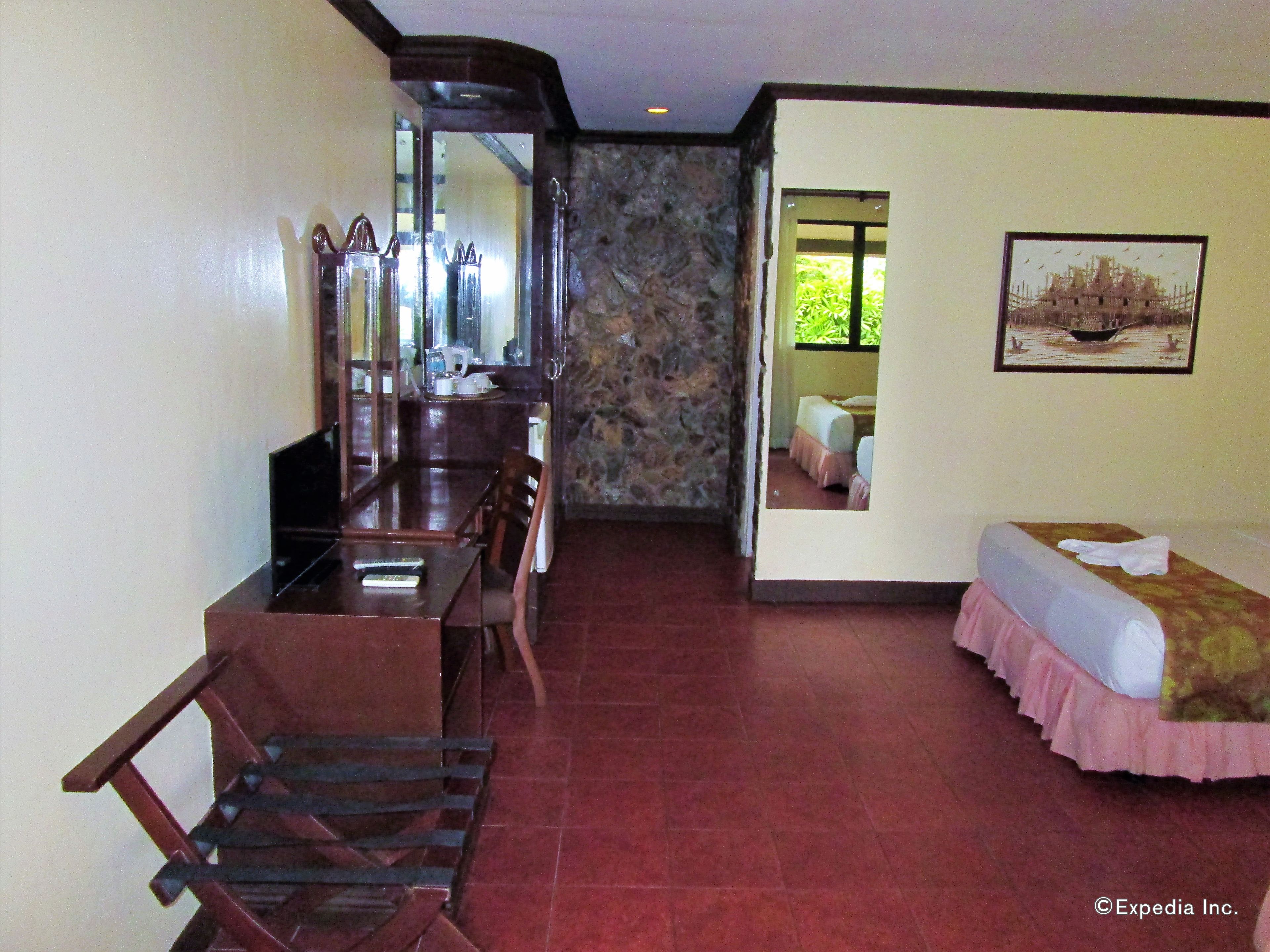 Quarto de hotel com área de jantar, cama e banheiro visível através de uma porta aberta.