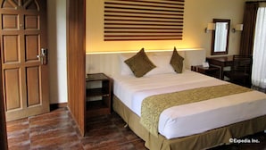 A hotel room with a large bed, a wooden door, a nightstand, a desk, and a mirror. - Chali Beach Resort and Conference Center (Cagayan de Oro)