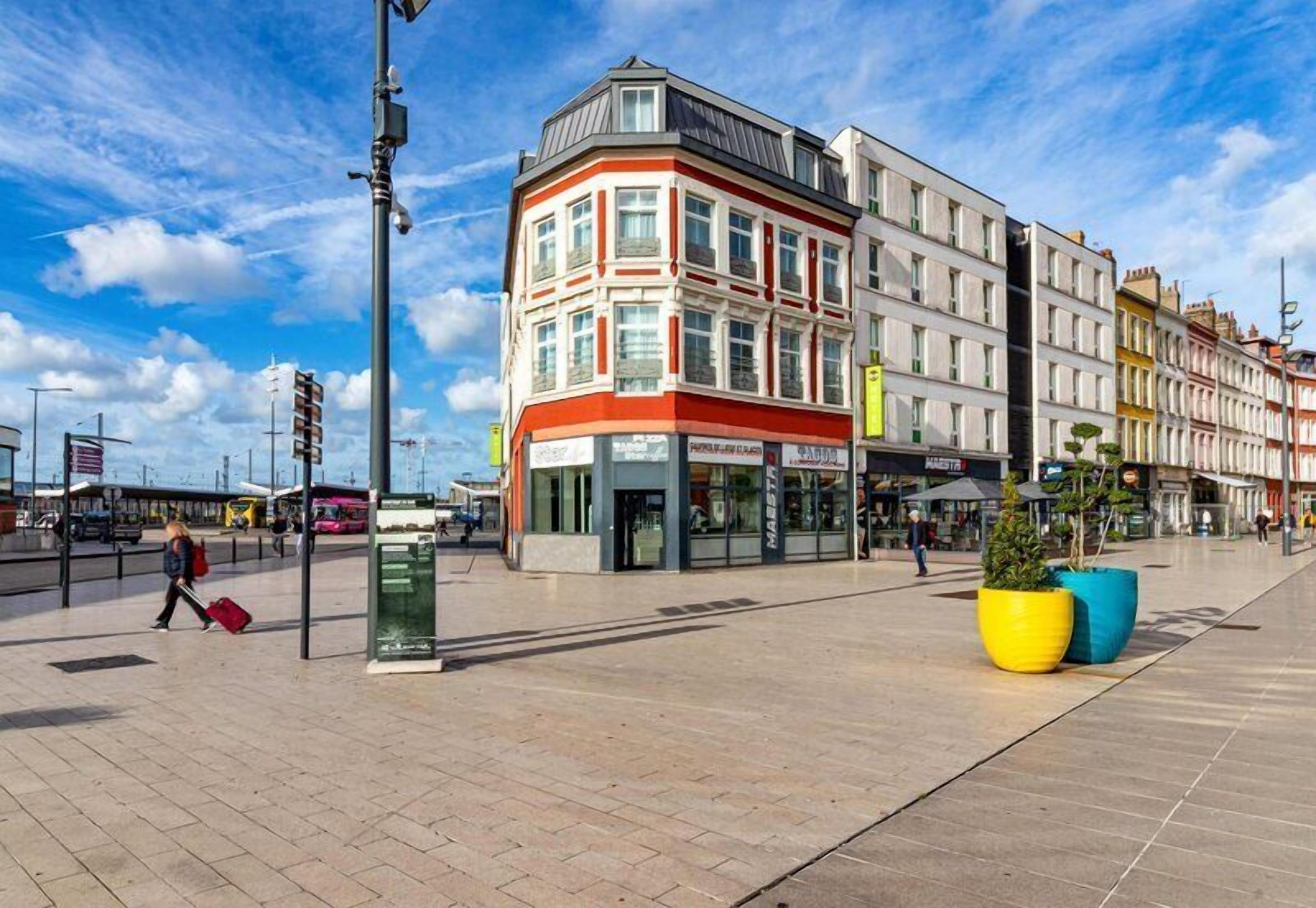 A public square with a modern building, a pedestrian walkway, and a bus stop.