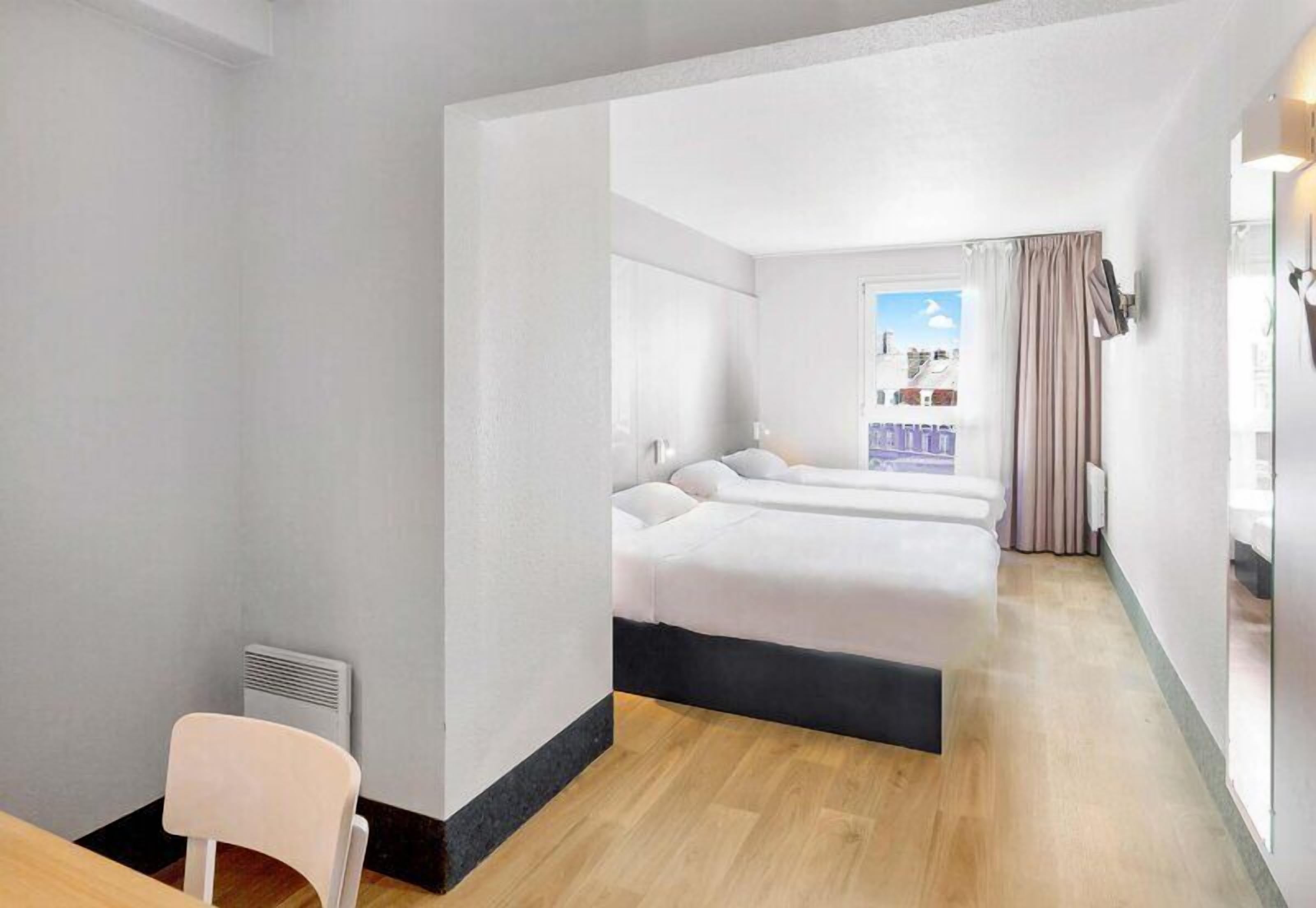 A hotel room with a bed, a chair, a window, and a view of the city.
