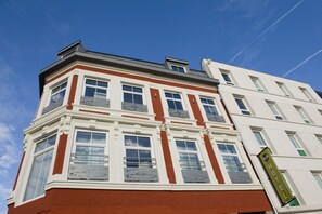 Un edificio en esquina con fachada roja y blanca, varios ventanales y un letrero que indica que es un hotel.