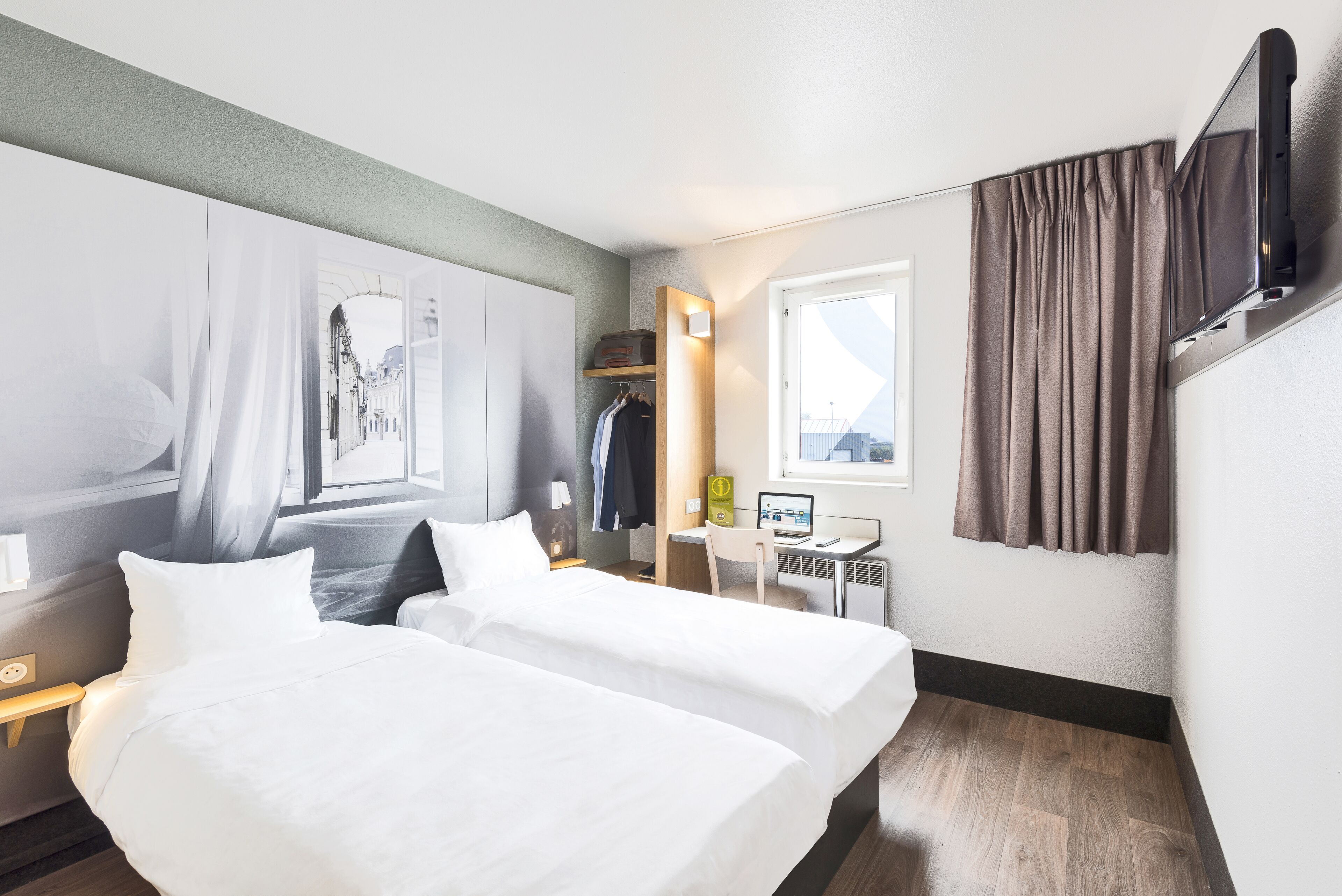 A hotel room with a bed, a desk, a chair, a wardrobe, and a TV mounted on the wall.