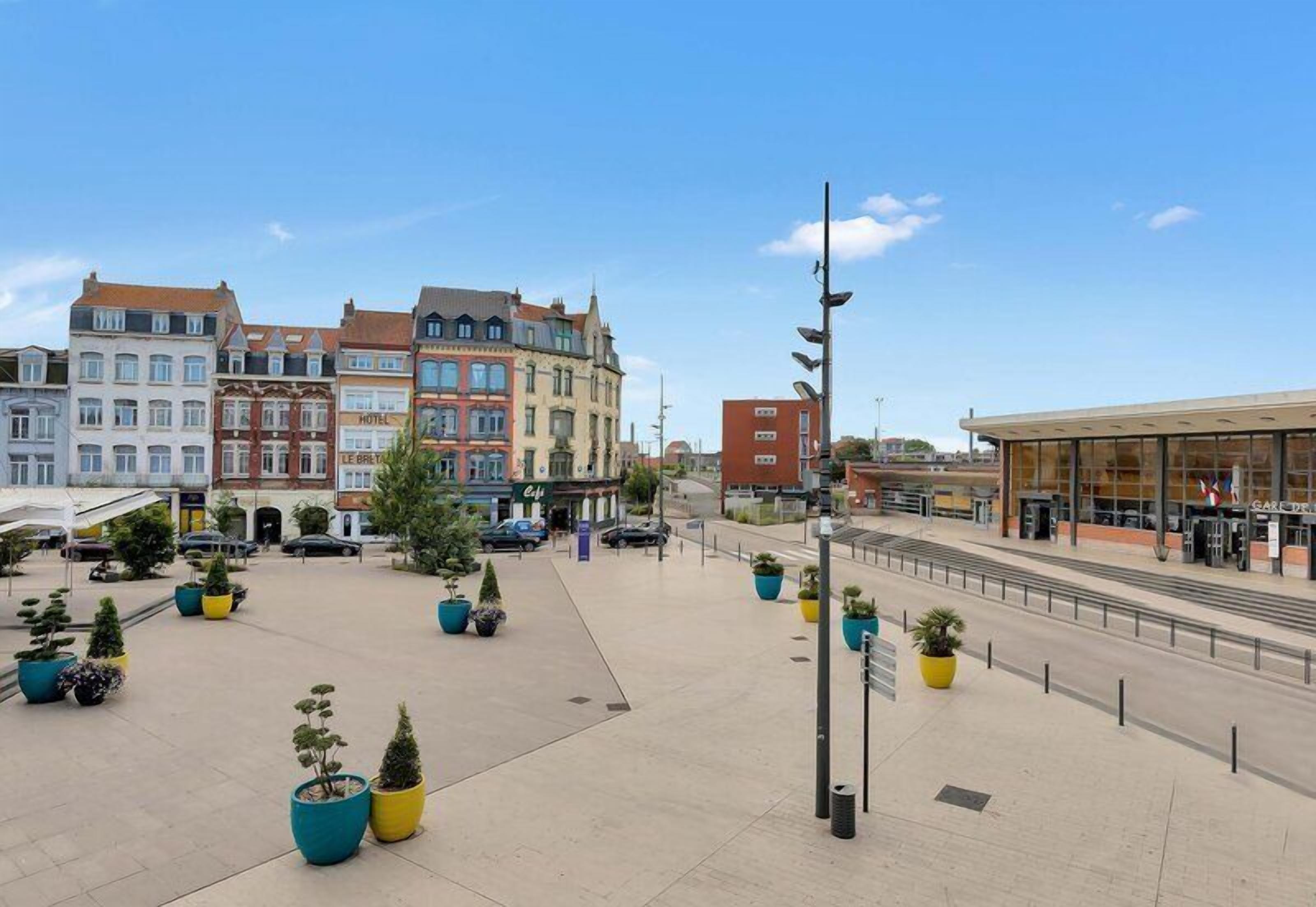 Una plaza pública con edificios, plantas en macetas y una estructura moderna.