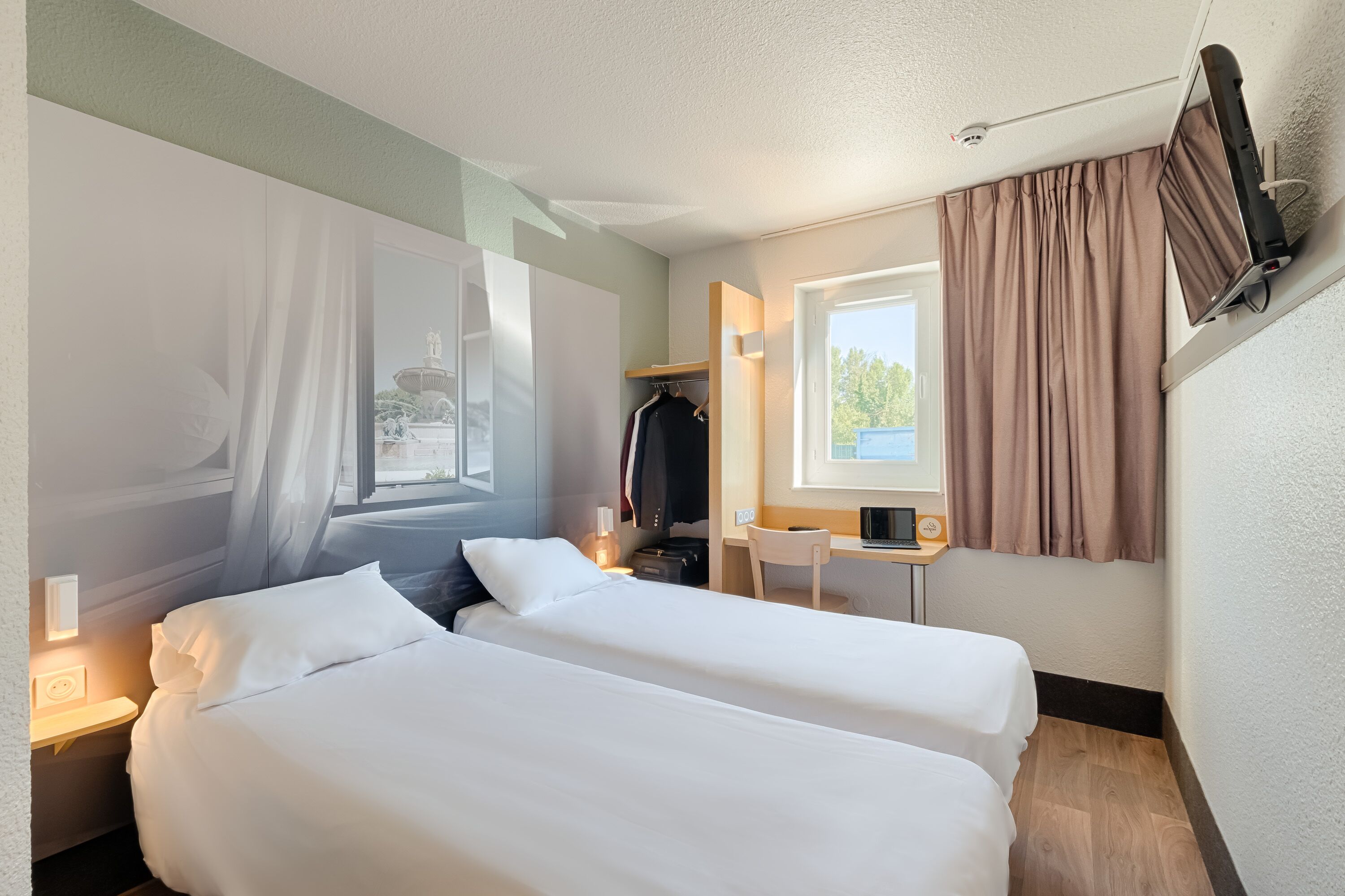 Habitación de hotel con dos camas, un escritorio, una silla, un armario y una ventana con cortinas.