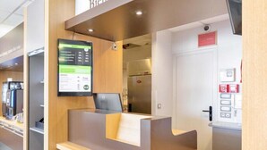 Una recepción con un mostrador de madera, una pantalla digital y una puerta con equipo de emergencia.
