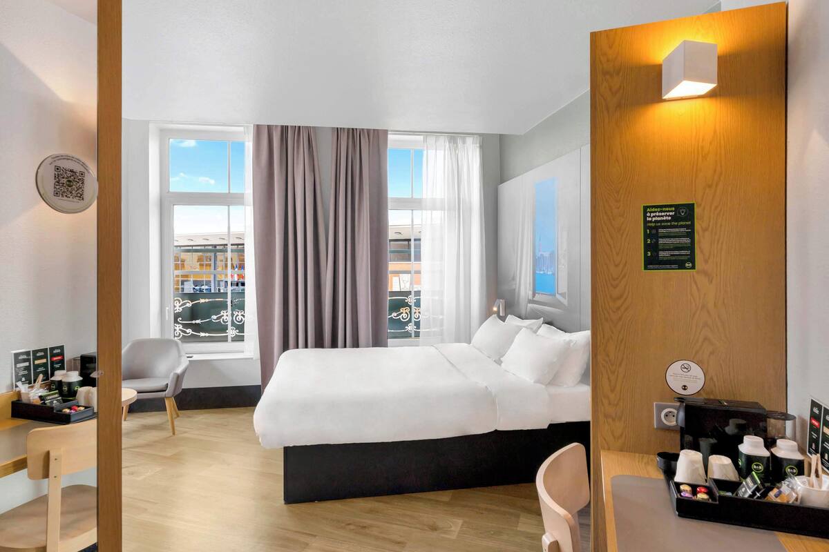 Hotellihuone, jossa on sänky, työpöytä, tuoli, kahvinvalmistuspaikka ja ikkuna, jossa on verhot.