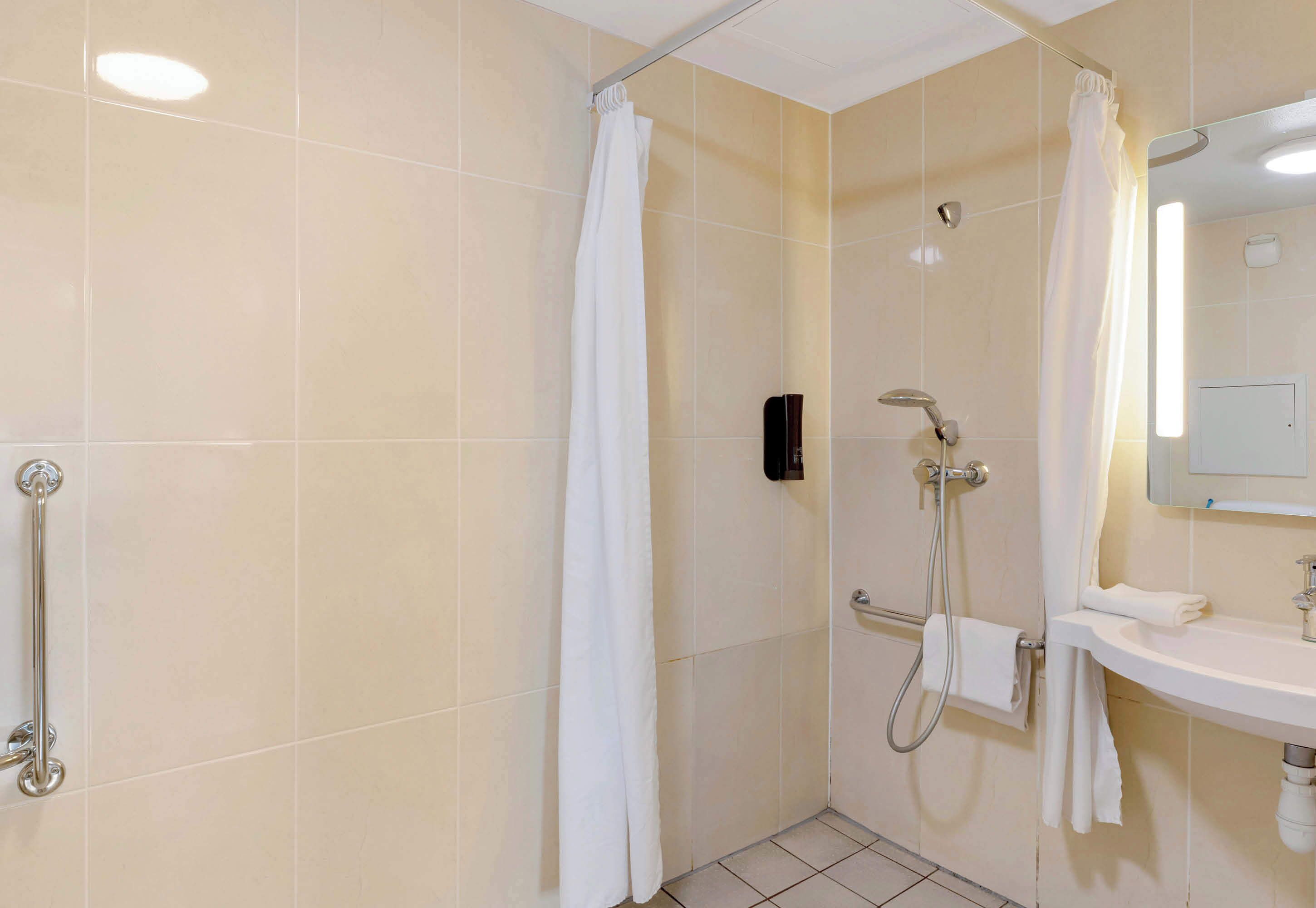 A bathroom with a shower, a handrail, a sink, and a mirror.