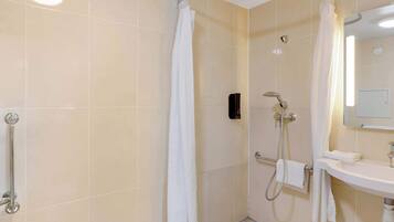 A bathroom with a shower, a handrail, a sink, and a mirror.