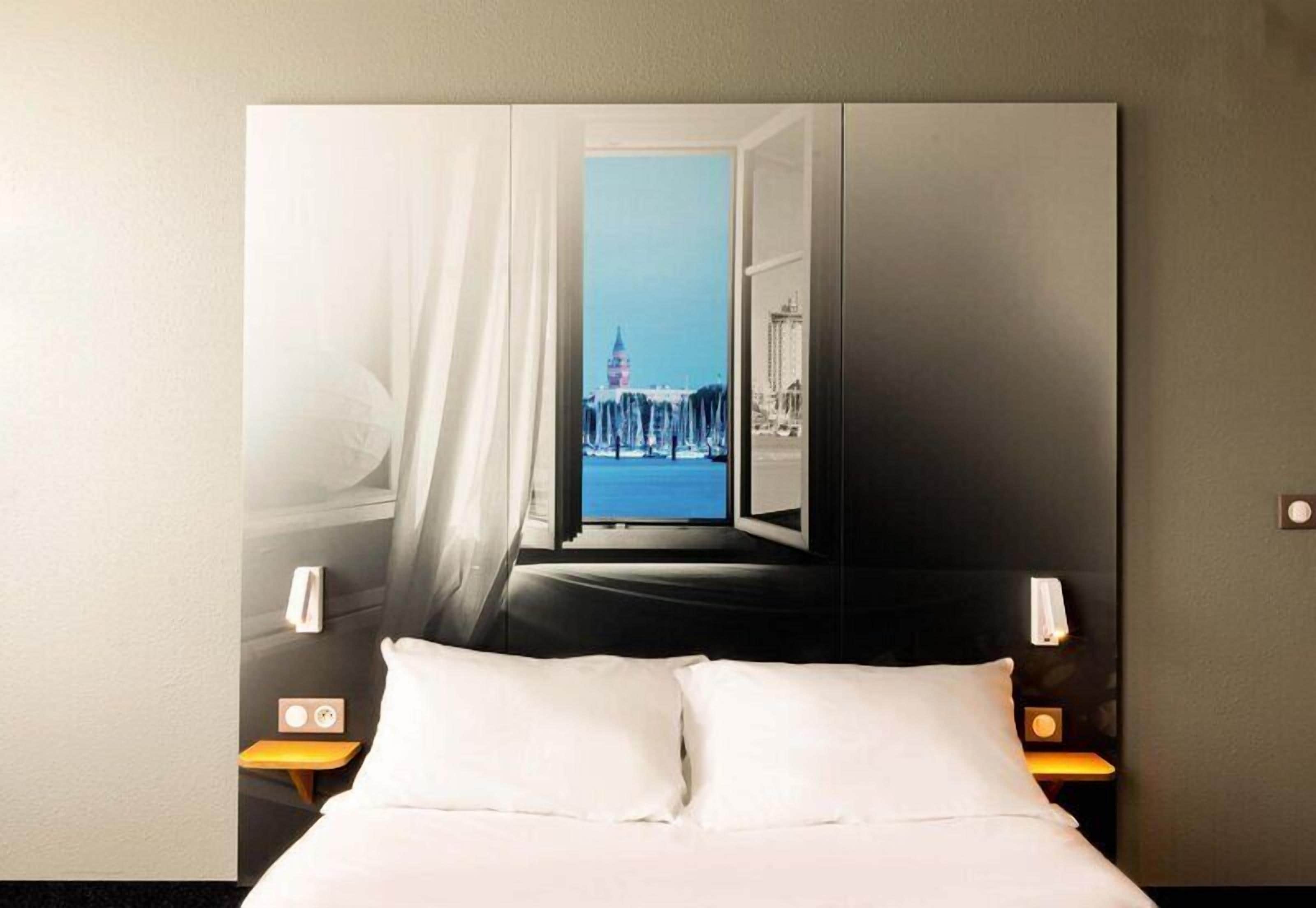 A hotel room with a bed, nightstands, and a large wall mural of a cityscape.