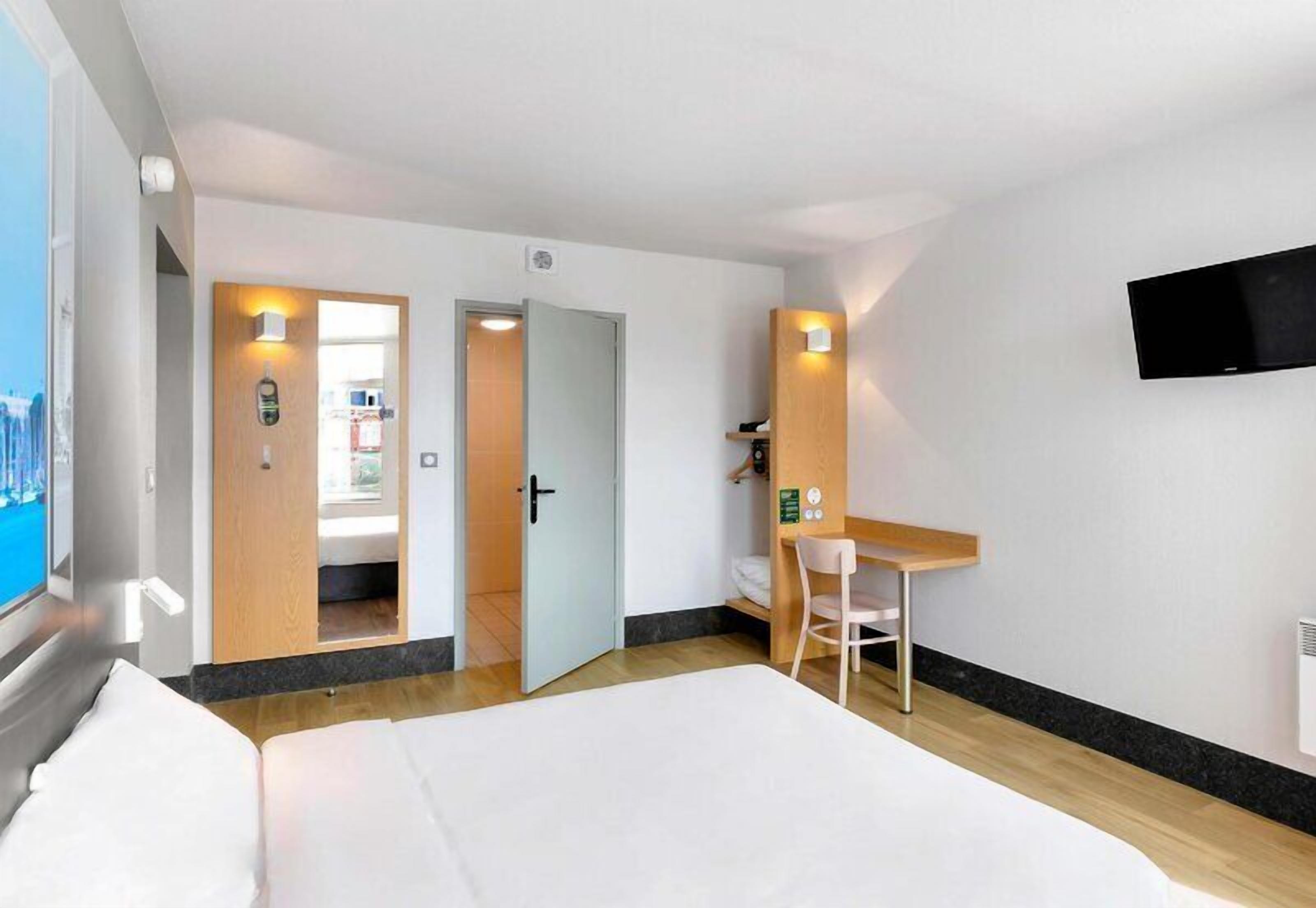 Una habitación de hotel con una cama, un escritorio, una silla, un televisor y una ventana.