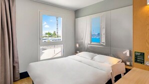 Habitación de hotel con cama, dos ventanas, un escritorio de madera y vistas a la ciudad.