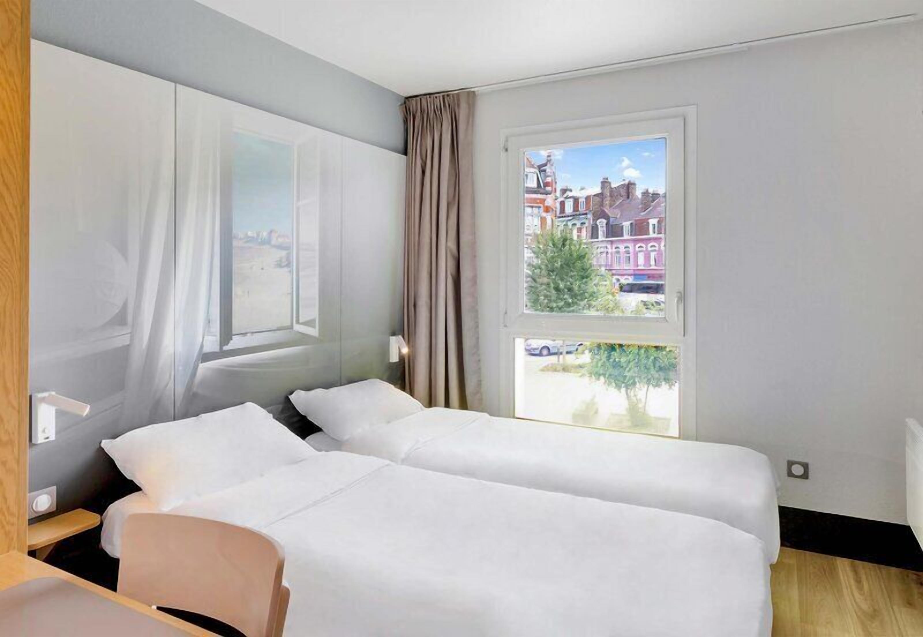 Habitación de hotel con dos camas, una ventana con vistas a edificios, un escritorio y una silla.