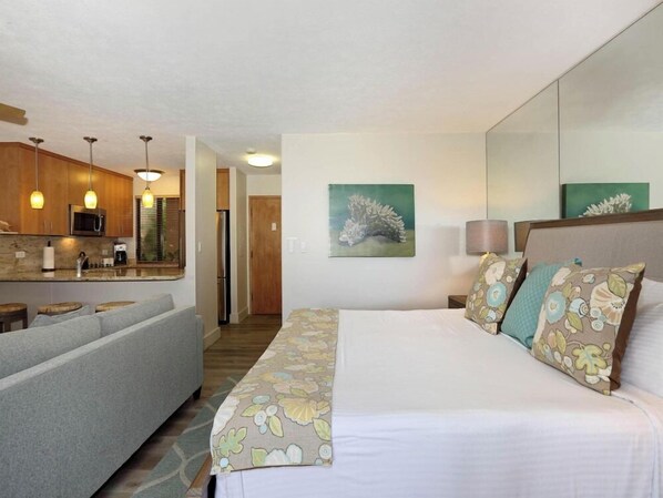 A hotel room with a bed, a sofa, a kitchenette, and a painting on the wall.