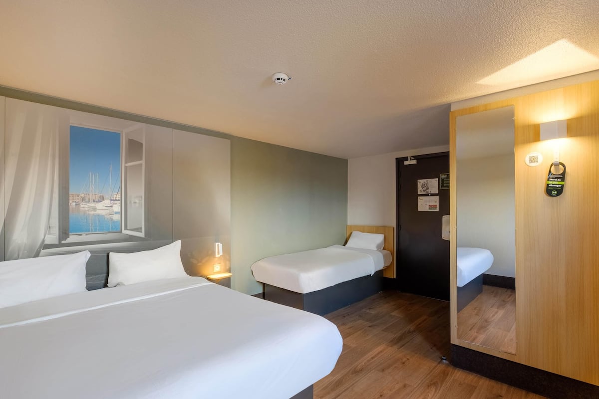 Une chambre d’hôtel avec deux lits, un grand miroir, une vue sur les bateaux par la fenêtre et un code QR sur le mur.