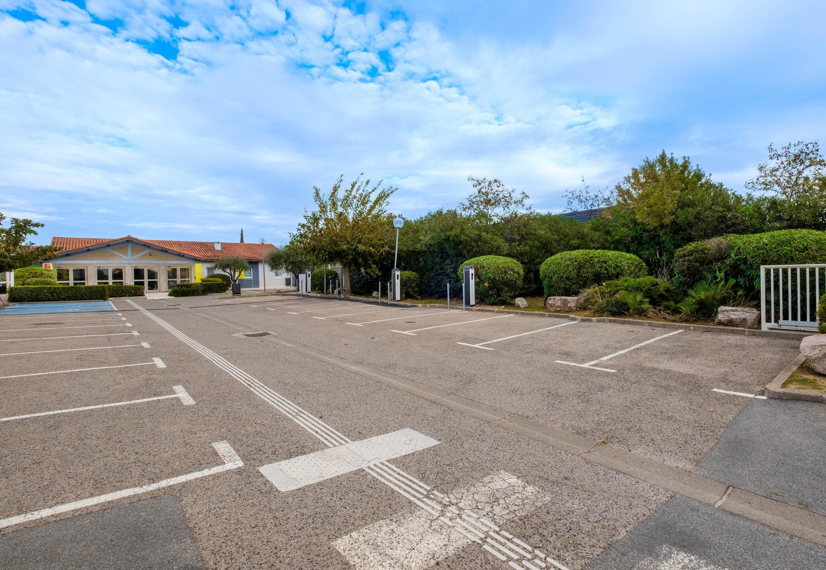 A parking lot with marked spaces, a building with a red roof, and surrounding greenery.