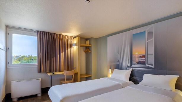 Ett hotellrum med två sängar, ett skrivbord, en stol, ett element och en tavla som föreställer en solnedgång över havet.