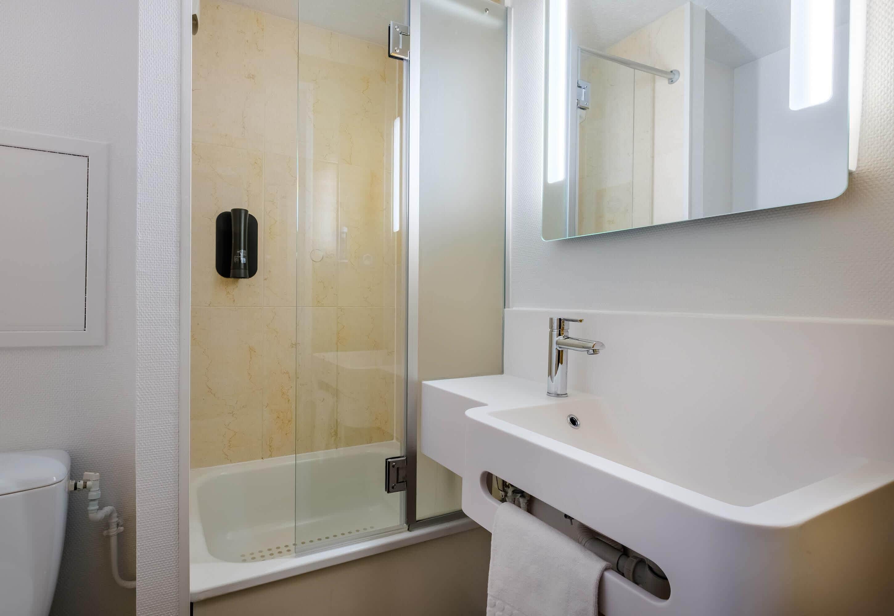 Une salle de bain moderne avec une douche à parois de verre, un lavabo blanc et un miroir au-dessus.