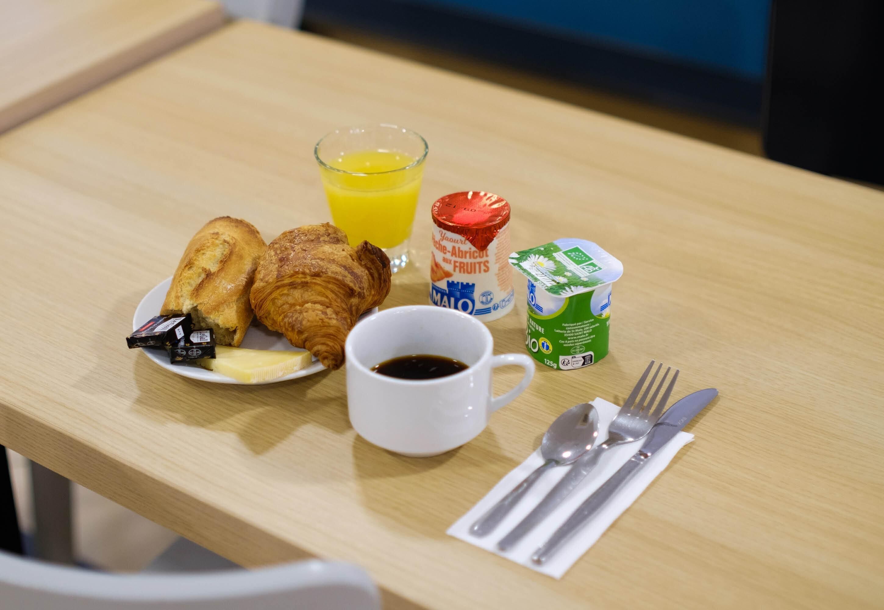 A breakfast setting with croissants, orange juice, yogurt, and a cup of coffee on a wooden table.
