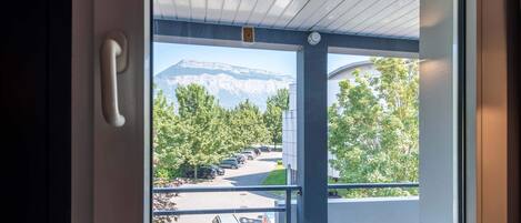 A window with a view of a parking lot, trees, and a mountain in the background.