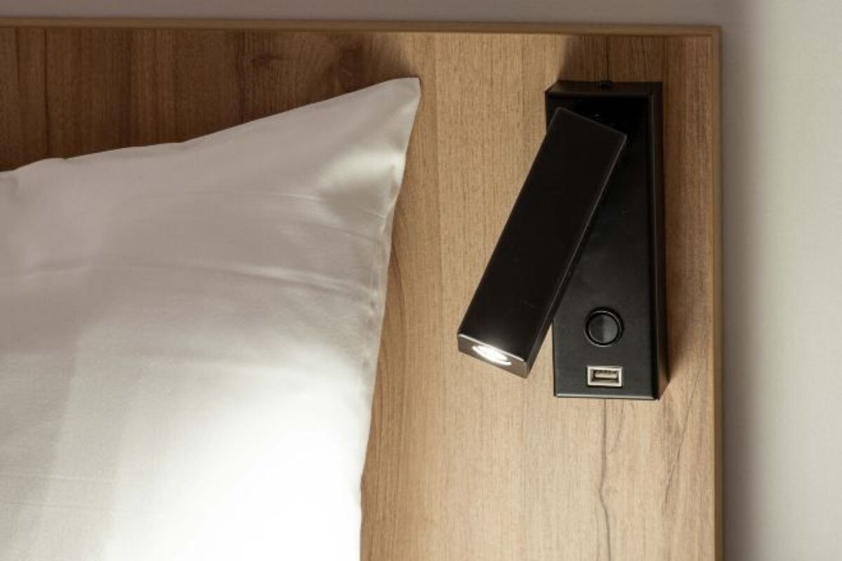 A bed with a white pillow and a black bedside table with a USB port.