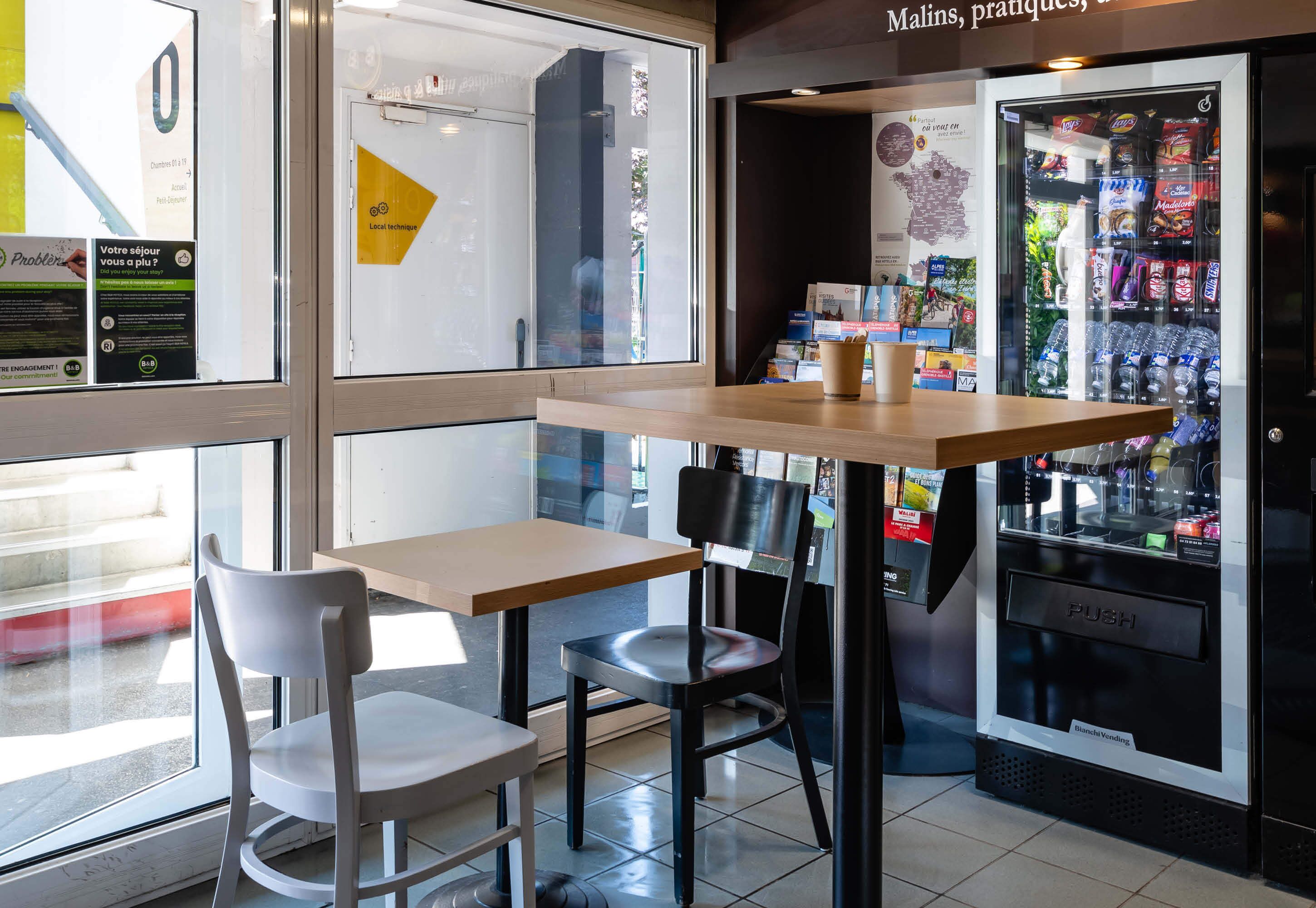 A seating area with a table and chairs, a vending machine, and a window with a view of the outside.