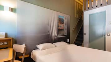 Une chambre d’hôtel avec un lit, un bureau et une chaise, un tableau au mur et un escalier.