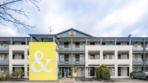 Un hôtel moderne, reconnaissable à son grand panneau jaune et blanc, qui s’étend sur plusieurs étages et dispose d’un parking.