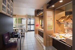 Zona de desayuno tipo buffet con diferentes opciones de comida y un área de estar con mesas y sillas.
