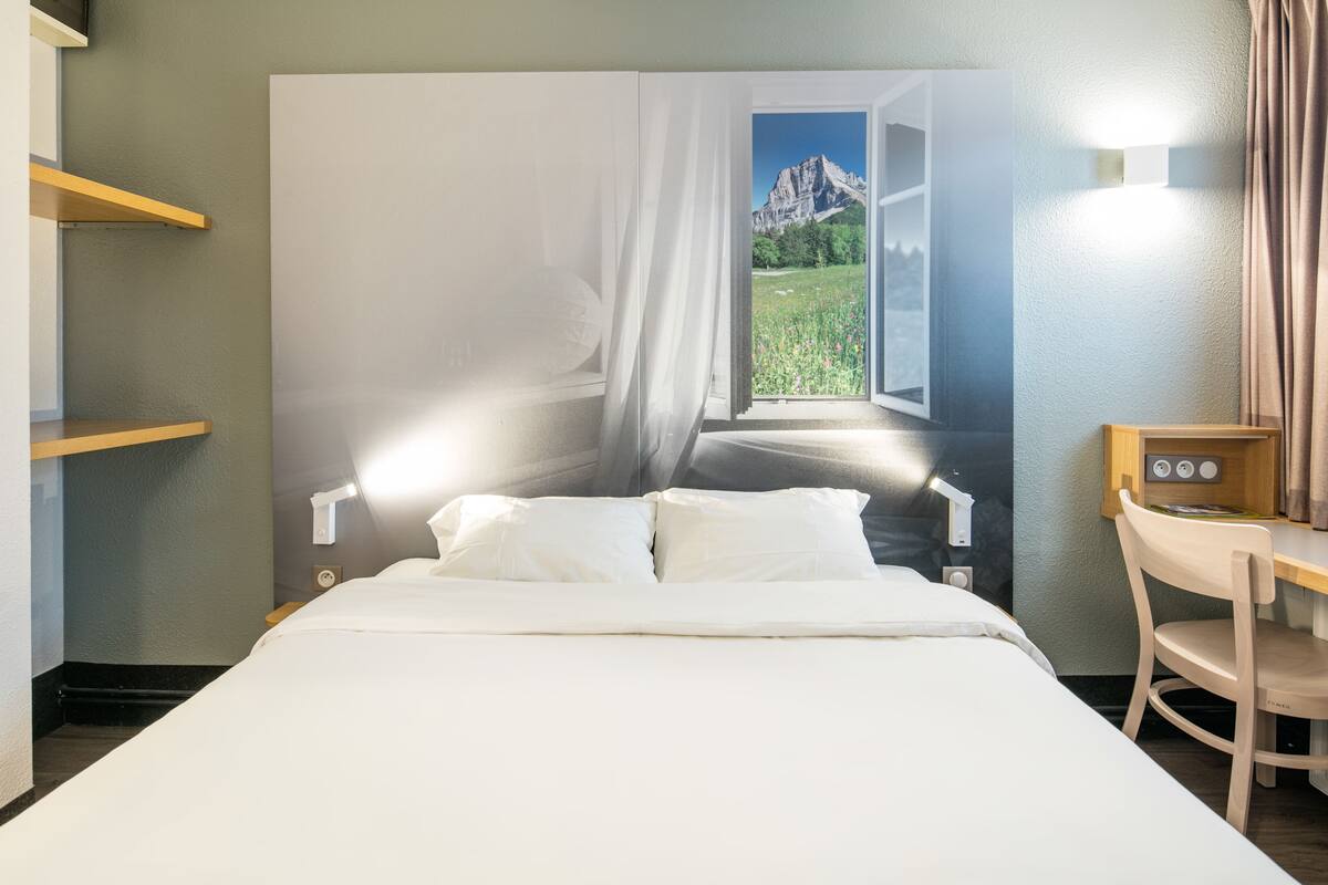 A hotel room with a bed, a desk, and a chair. There is a window with a view of mountains.