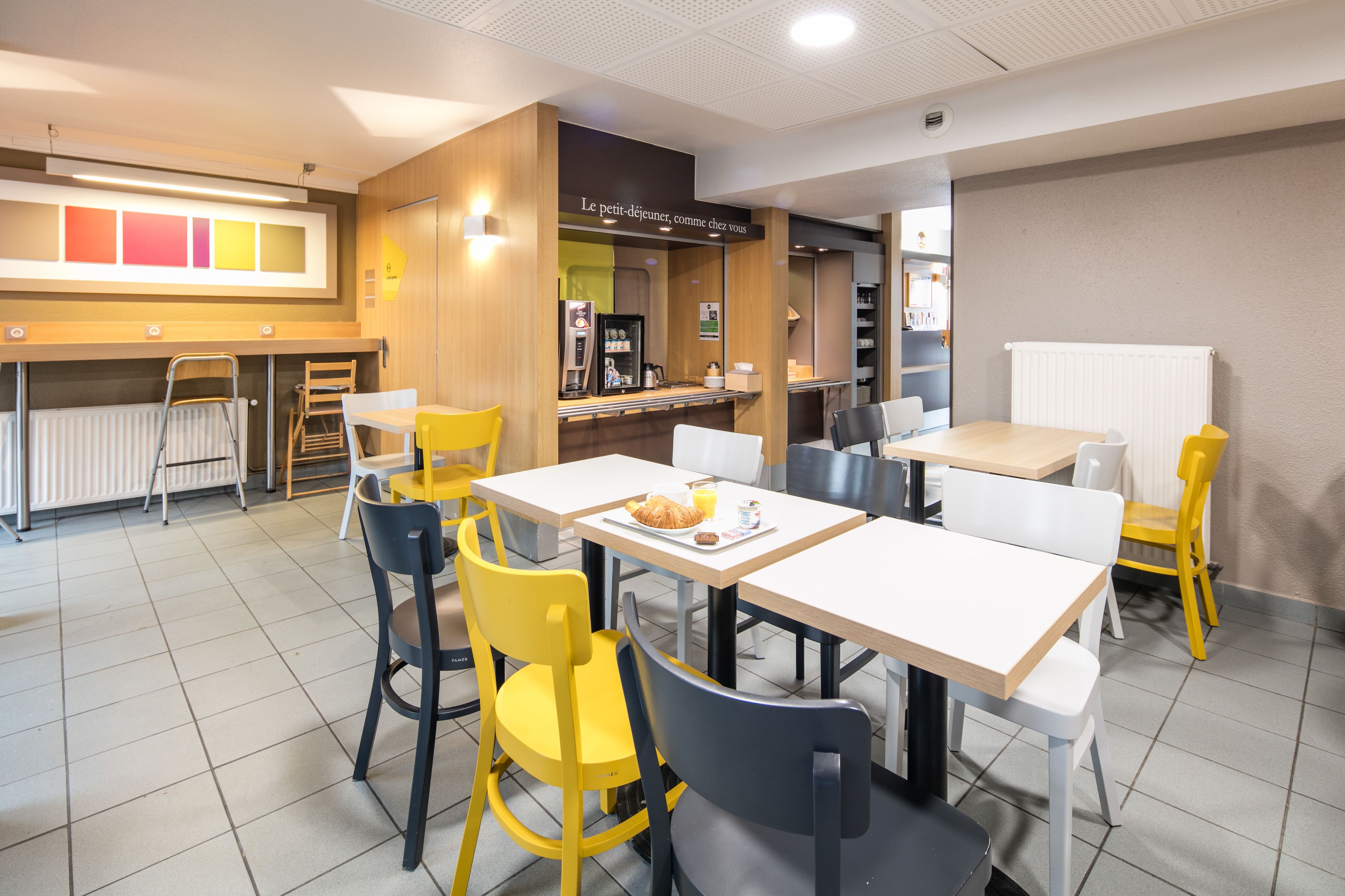 A modern dining area with yellow and gray chairs, white tables, and a visible counter with a menu.