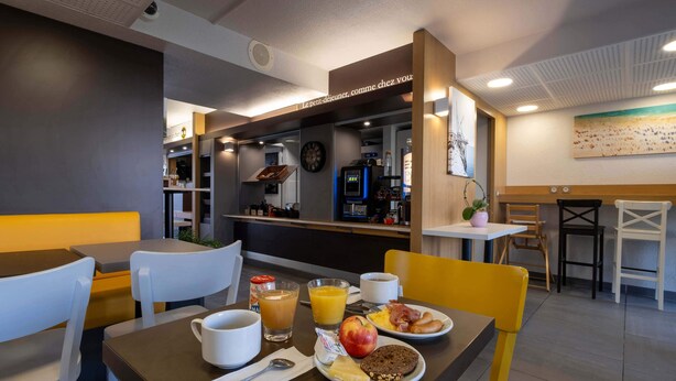 A breakfast setup with a coffee machine, fruit, and eggs on a table in a modern cafe. - B&B HOTEL La Rochelle Angoulins-sur-Mer (Angoulins)