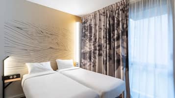 A hotel room with two beds, a wall art piece, a nightstand with a lamp, and sheer curtains.