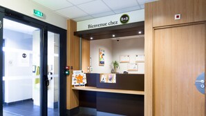 A reception area with a wooden desk, a sign reading "Bienvenue chez B&B Hotels," and a door with a glass panel. - B&B HOTEL LILLE Tourcoing Centre (Tourcoing)