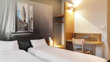 Une chambre d’hôtel avec deux lits, un bureau, une chaise, un porte-manteau et un tableau représentant un paysage urbain.