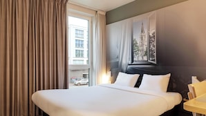 A hotel room with a large bed, a wooden floor, a window with curtains, and a wall-mounted picture. - B&B HOTEL LILLE Tourcoing Centre (Tourcoing)