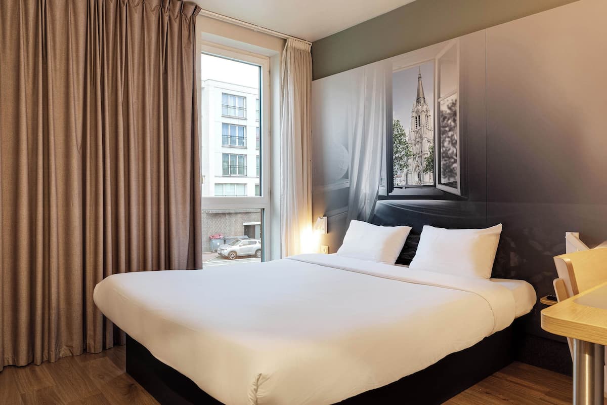Habitación de hotel con una cama grande, piso de madera, ventana con cortinas y un cuadro colgado en la pared.