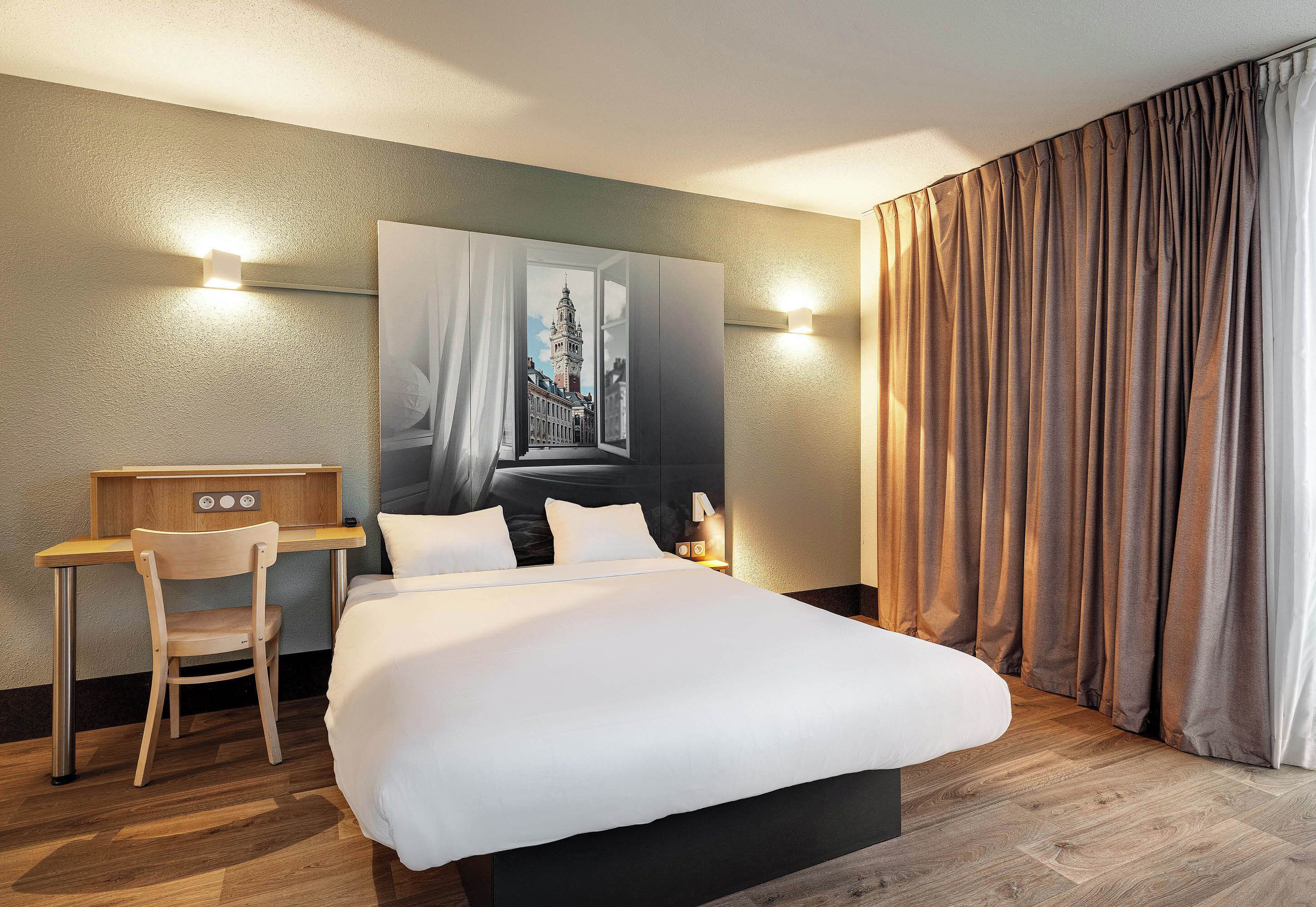 Een hotelkamer met een bed, een bureau, een stoel en een wandlamp.