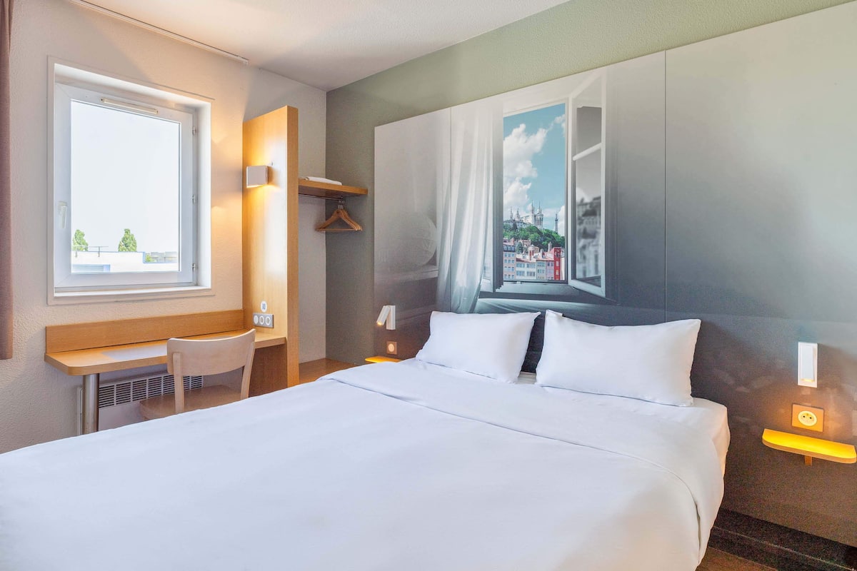 Une chambre d’hôtel avec un grand lit, un bureau, une chaise et une fenêtre donnant sur le paysage urbain.
