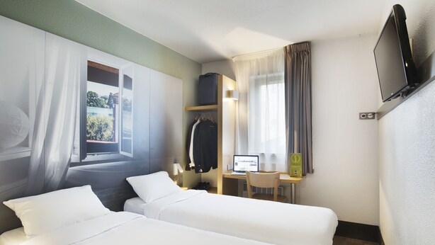 Une chambre d’hôtel avec deux lits, un bureau avec un ordinateur, une télévision et une fenêtre avec des rideaux.