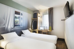 Une chambre d’hôtel avec deux lits, un bureau avec un ordinateur, une télévision et une fenêtre avec des rideaux.