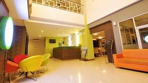 Un vestíbulo de hotel con mostrador de recepción, una escalera y un área de descanso con sillas coloridas.